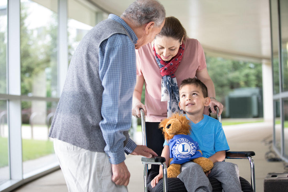 A childhood cancer patient holds a stuffed animal lion while smiling at an old man visiting him.